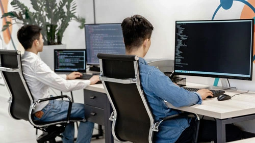 Two people writing code in an office